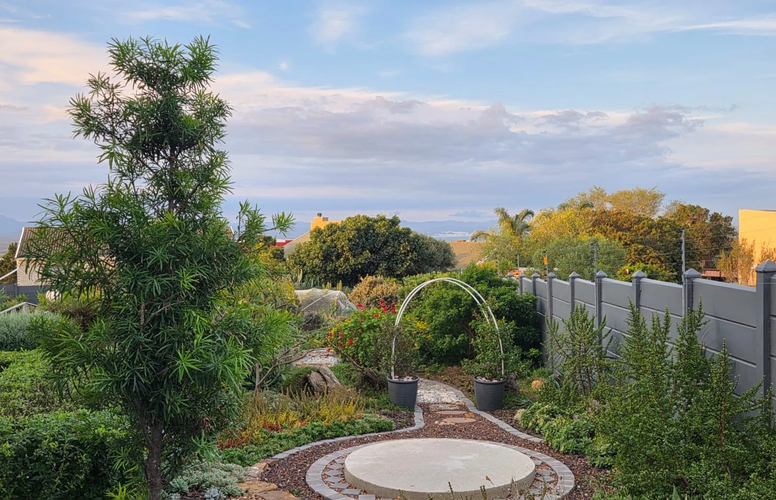 An indigenous coastal garden in Jeffreys Bay with a round paved feature, a garden arch and fynbos planting