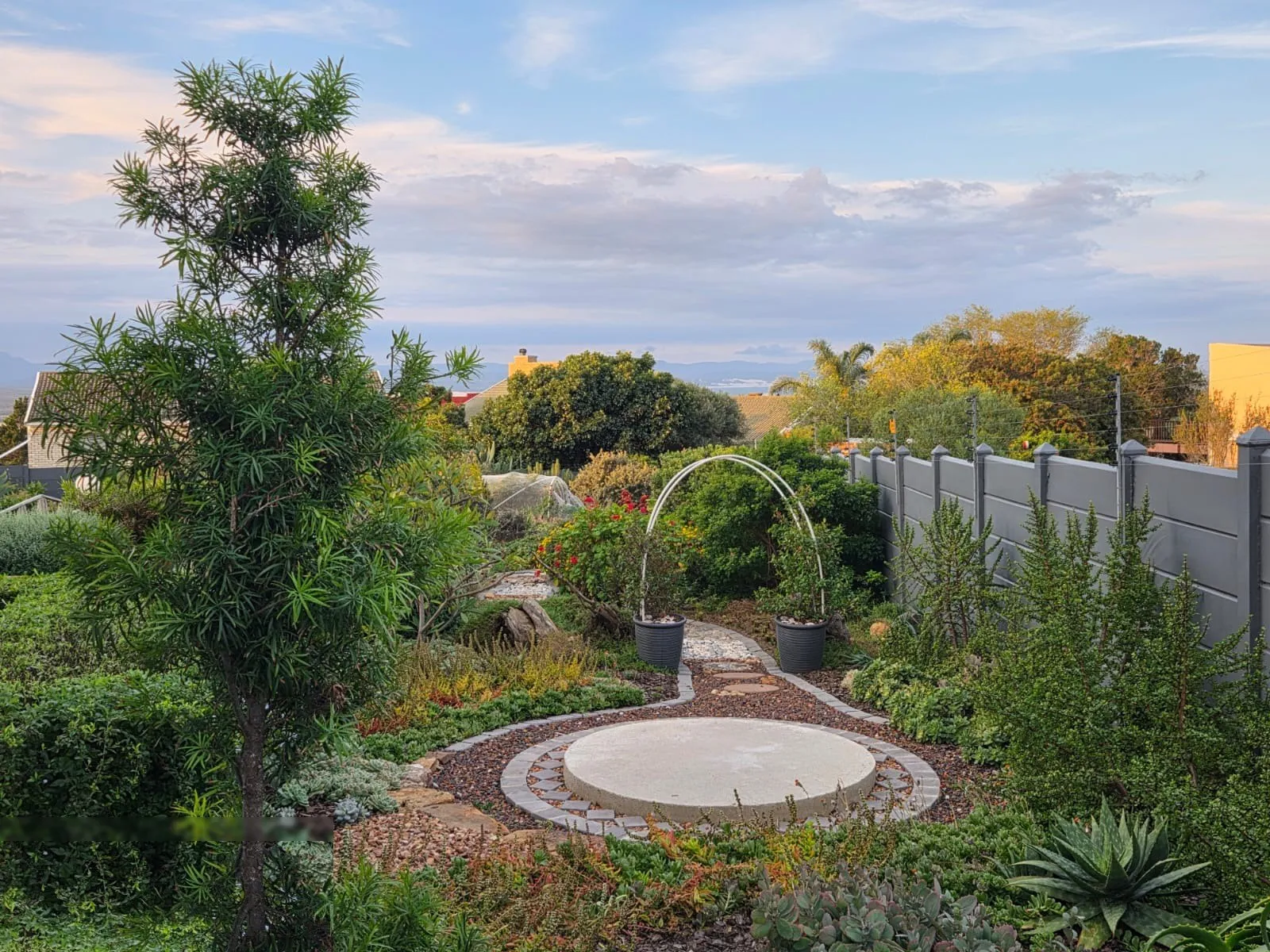 An indigenous garden with a round paved feature, a garden arch and coastal planting